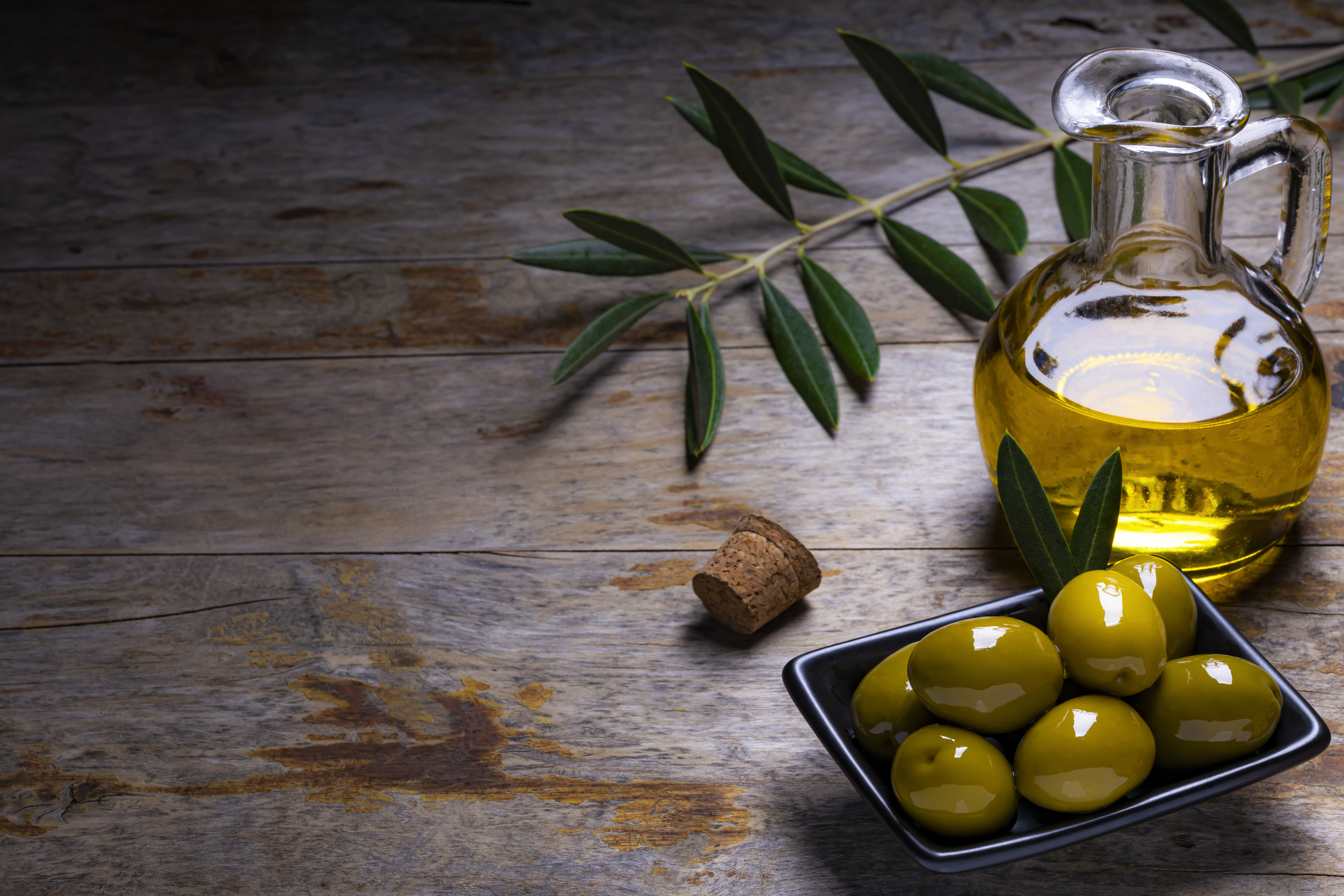 Tasty looking olives extra virgin olive oil and olive leafs on dark wooden background.