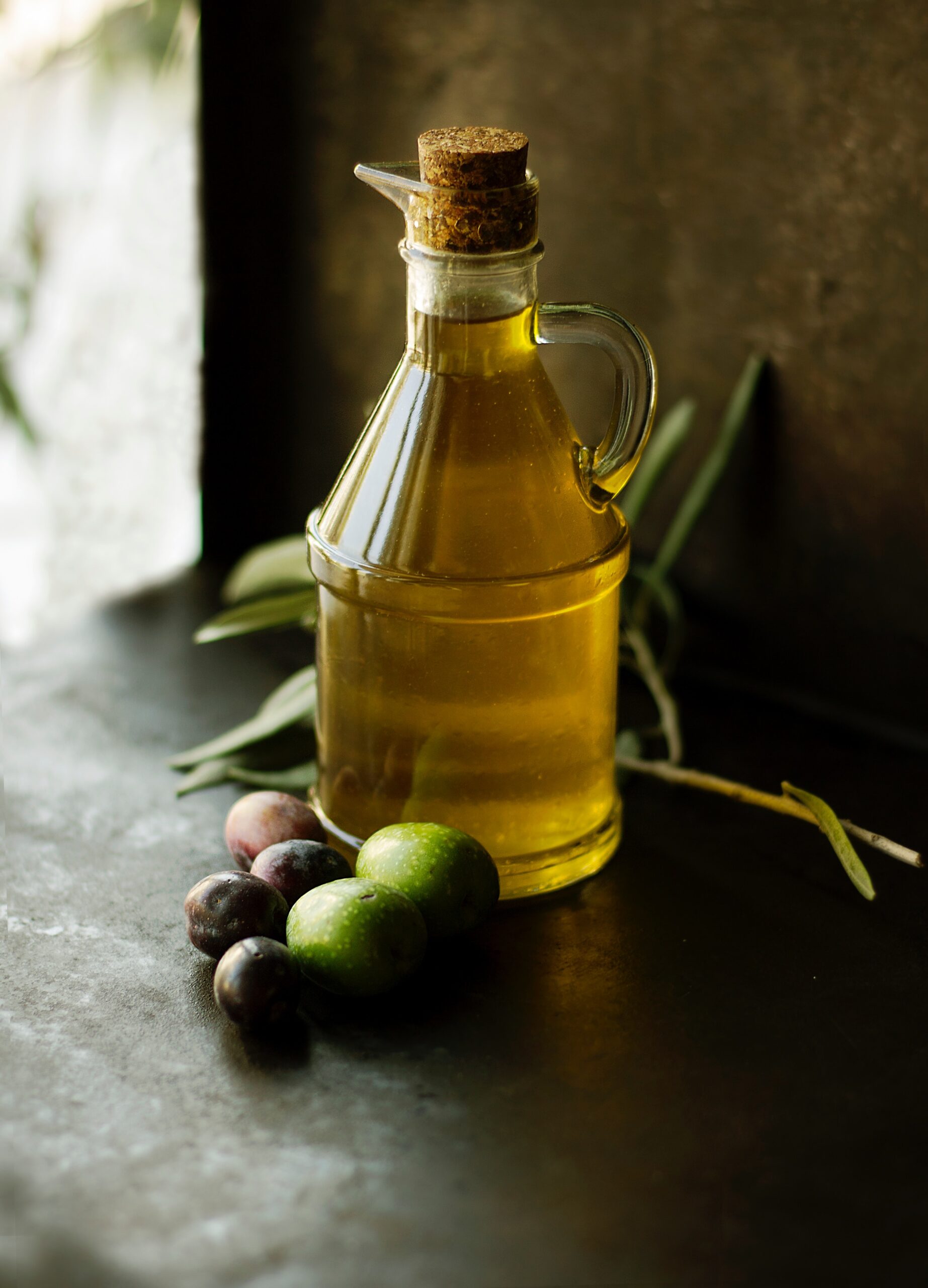 Rami di olivo carichi di olive al tramonto, con un borgo collinare sullo sfondo